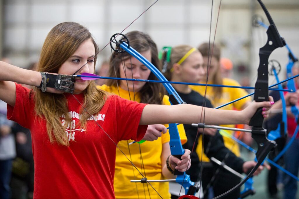 Girl in line of archers at NASP state tournament taking aim with her bow and arrow.