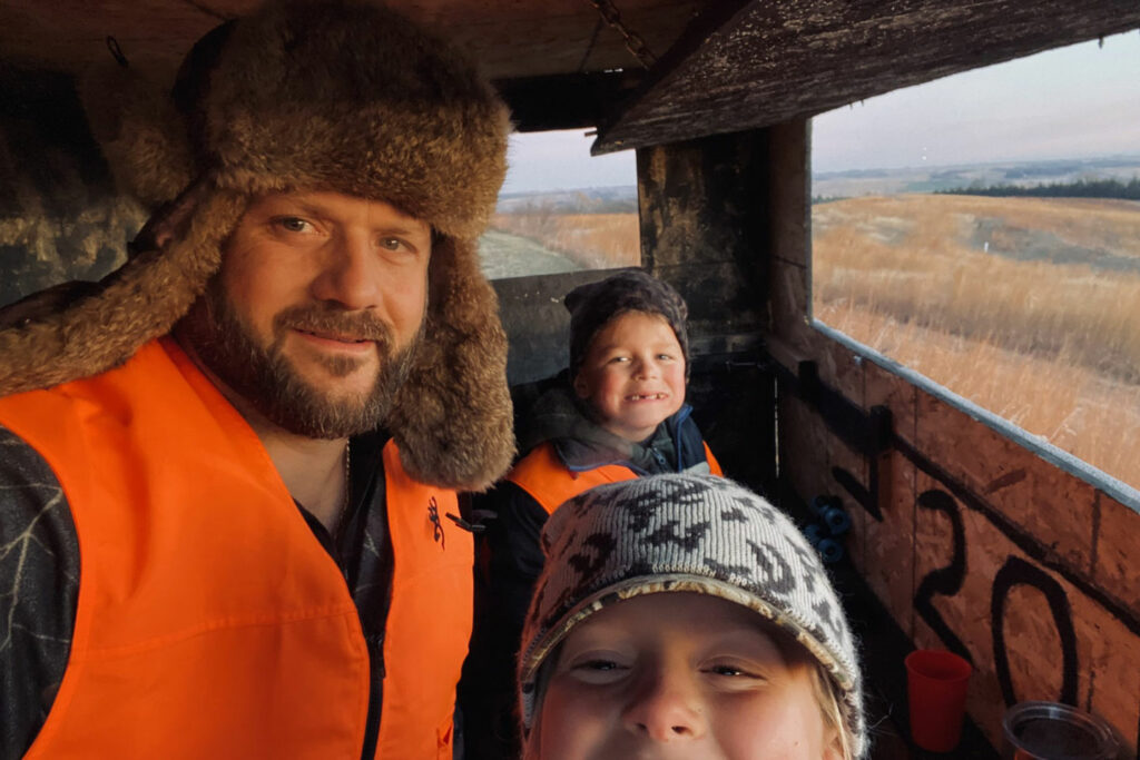 A father and two children take a selfie in a hunting blind.