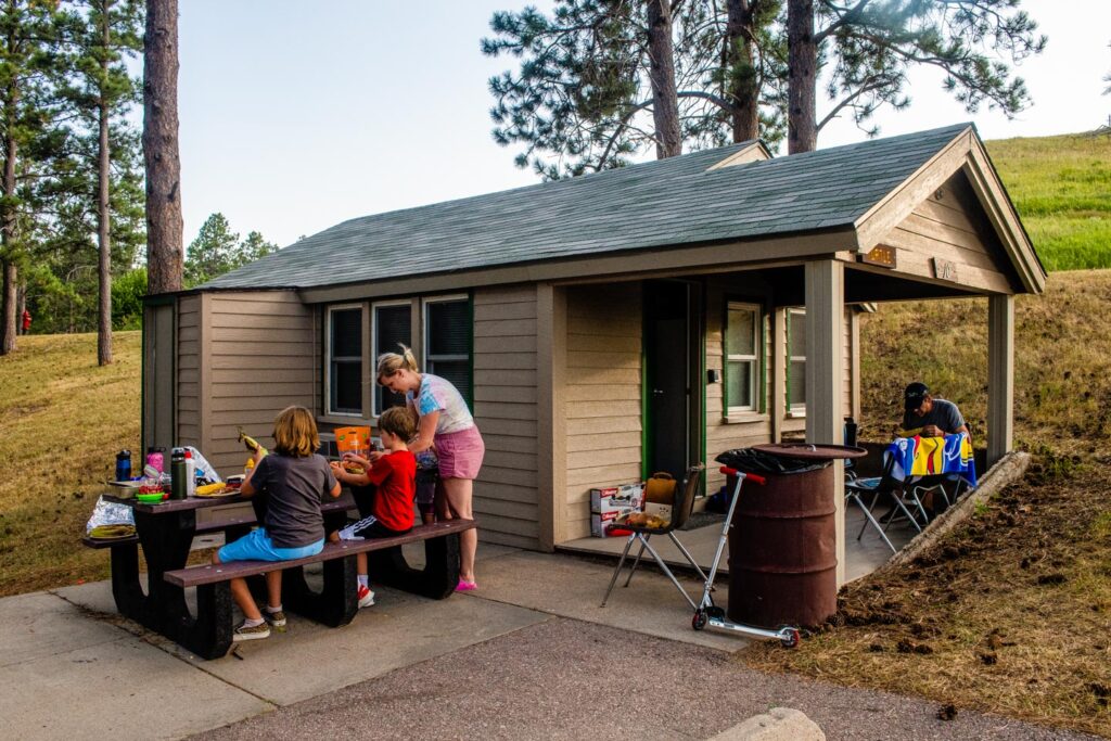 Park guests picnic next to a cabin at Chadron State Park in Dawes County. Copyright Nebraskaland Magazine/Nebraska Game and Parks Commission.