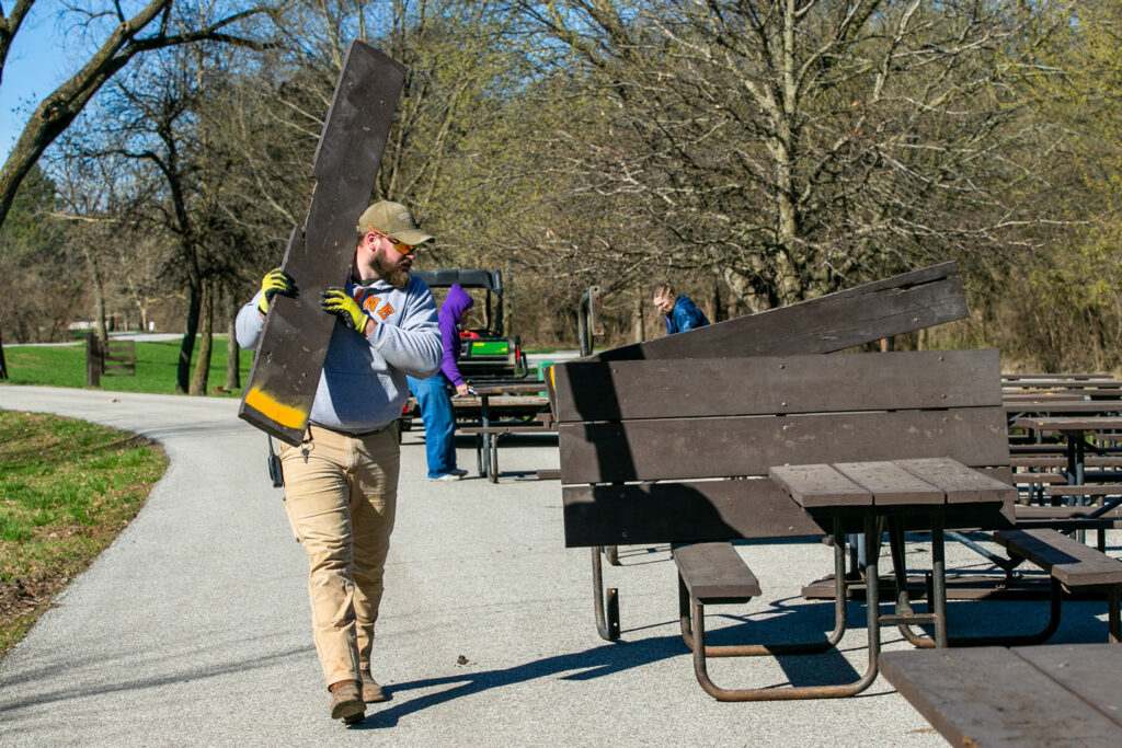 A park worker carries part of a picnic table while making bench repairs
