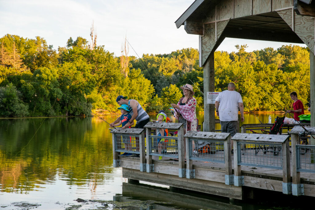 Justin and Ella Heckel of Omaha fishing with their sons Zalen (blue shirt) and Judah. People fishing on the fishing pier at Louisville State Recreation Area. Nguyen-Wheatley, June 27, 2020. Copyright Nebraskaland Magazine, Nebraska Game and Parks Commission.