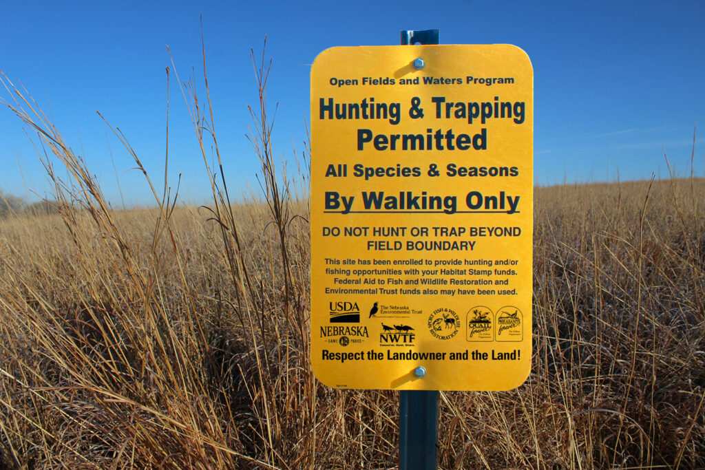 Open Fields and Waters (OFW) Program signage at a wheat field OFW site great for upland game bird habitat. Sign reads "Hunting and Trapping Permitted"