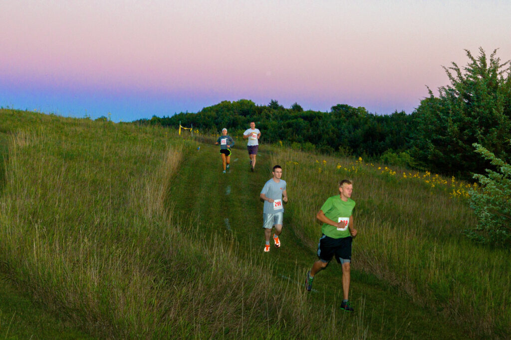People run down a grassy trail at sunset during the Night Owl 5K run at Niobrara State Park.