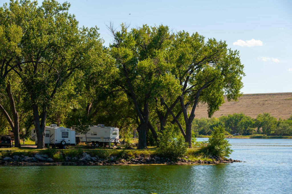 Campers are parked in a campground shaded by trees at Lake Ogallala SRA.