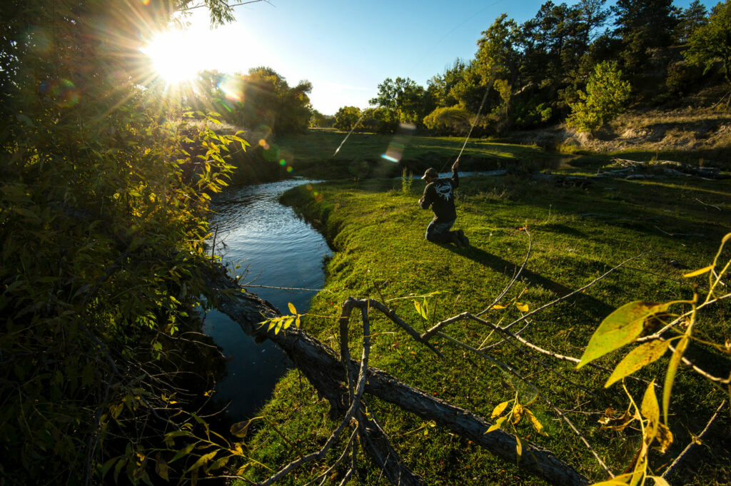 A man fly fishes on private land near a winding stream during the fall