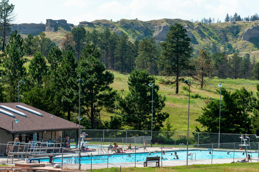 Swimmers cool off on a hot day at Chadron State Park with pine trees and buttes in the background scene.