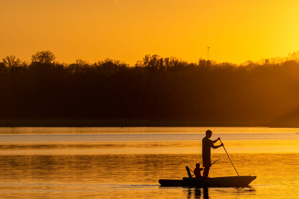 A parent and their child paddle the waters of Conestoga Lake as the sun descends across the horizon.