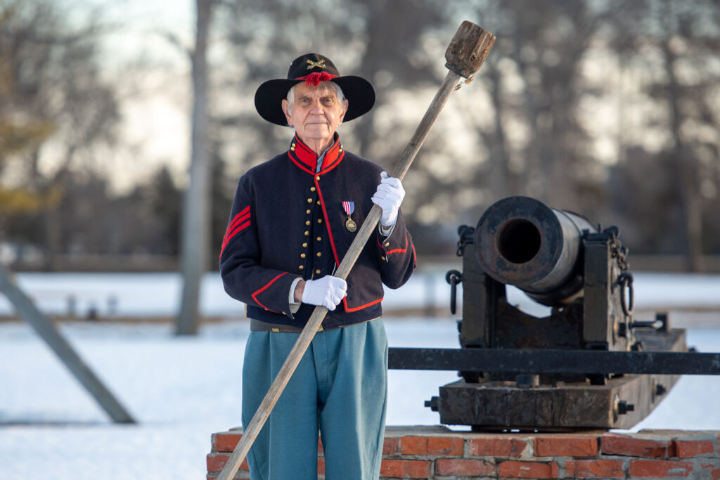 A man in period clothing stands in front of a cannon