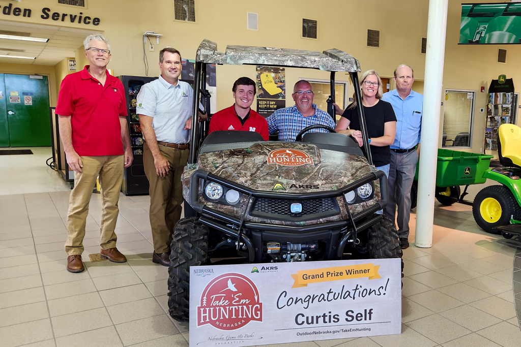 Five people pose with a grand prize John Deere gator utility vehicle.