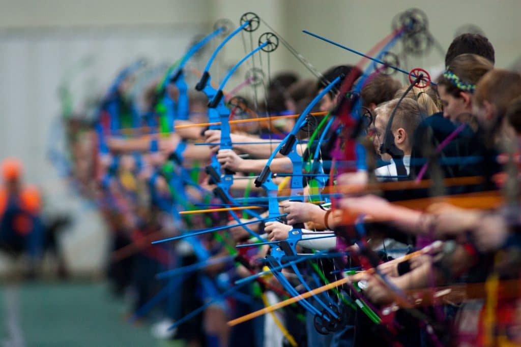 high school students line up to shoot archery at an indoor archery tournament