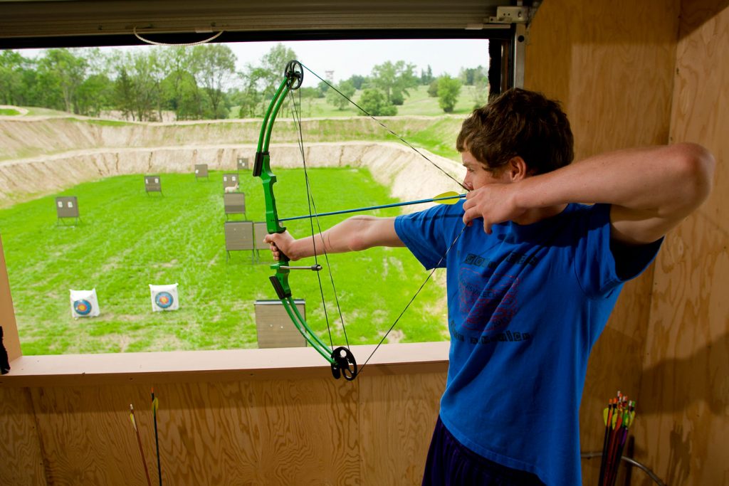 A boy shoots arrows at targets from an elevated archery tower at a state park.