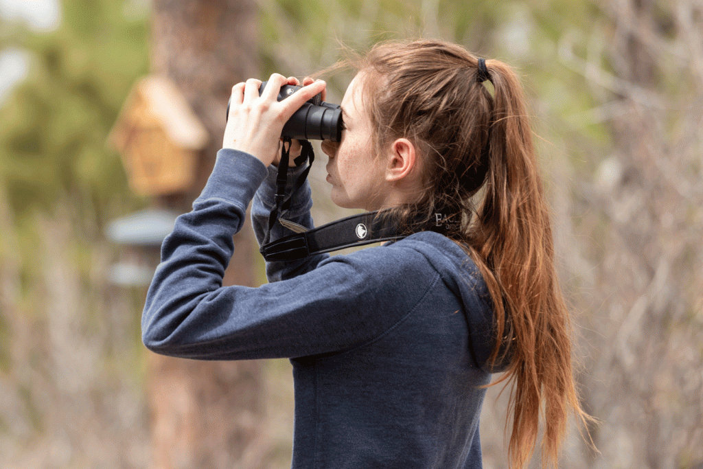 A girl with red hair looks through binoculars