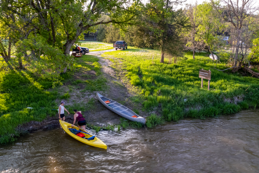 two women pull a kayak from the river; a canoe sits on the bank