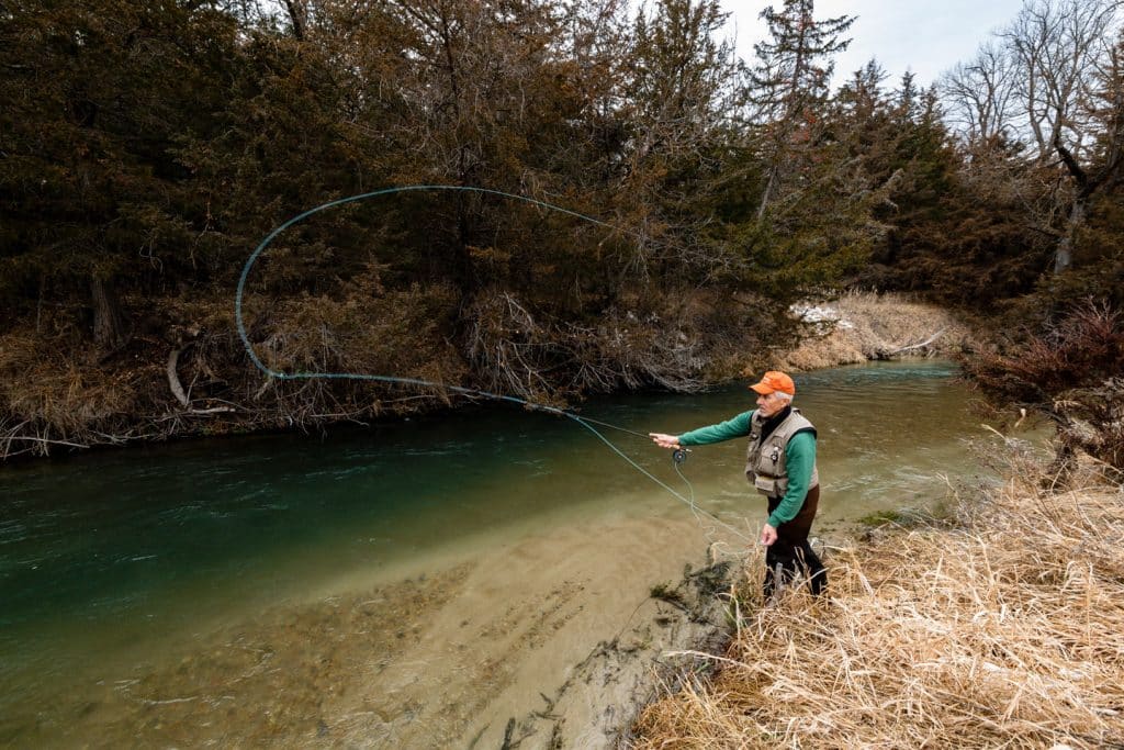 A man fly fishes for trout during December along a winding, tree-lined creek at Pine Glen WMA in Nebraska