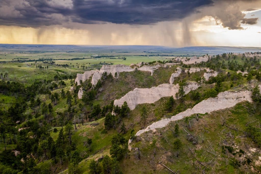 Rugged landscapes at Ponderosa Wildlife Management Area stand in the foreground as a thunderstorm moves over the Pine Ridge near Fort Robinson State Park.
