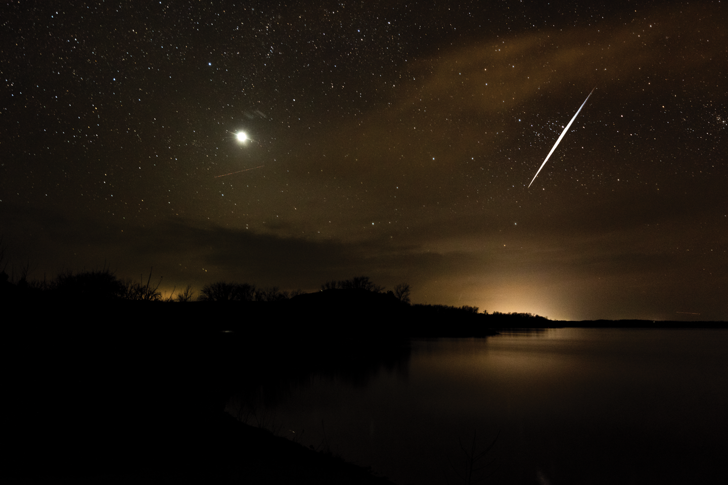 a shooting star makes a white streak across a very dark sky