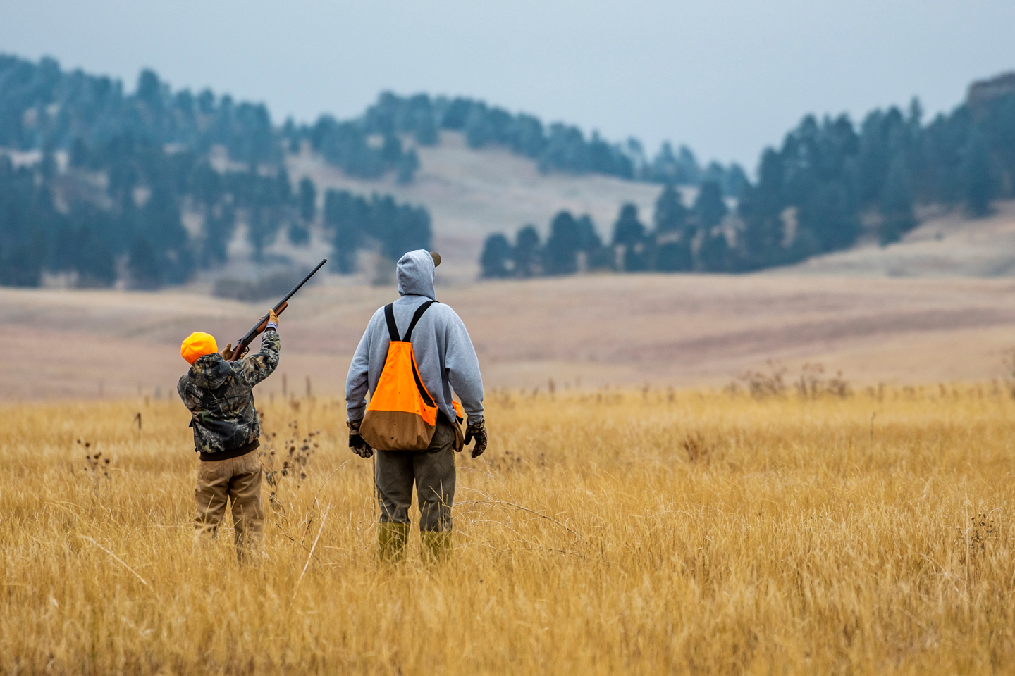 a young boy shoots at a pheasant, his dad standing beside him