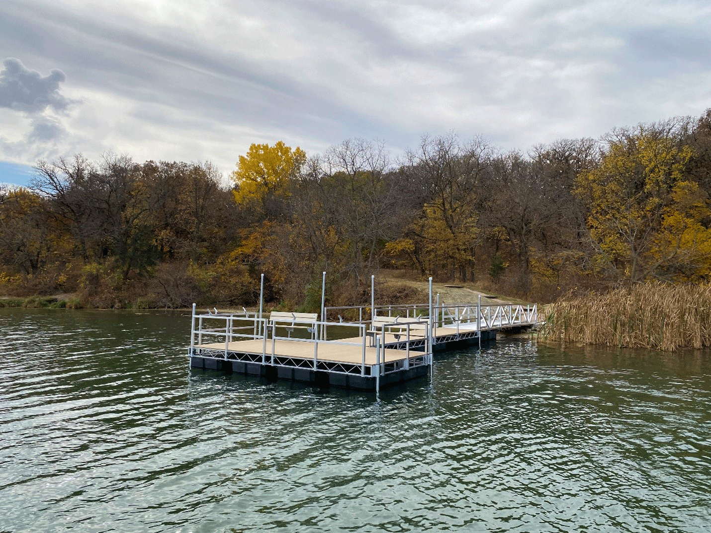 a new pier hangs over blue water with fall trees in the background