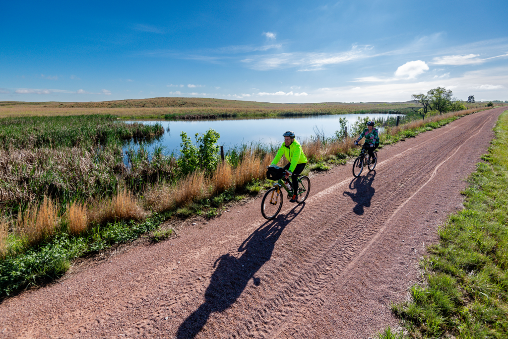 Two people ride bikes on a dirt path through Nebraska Sandhills.