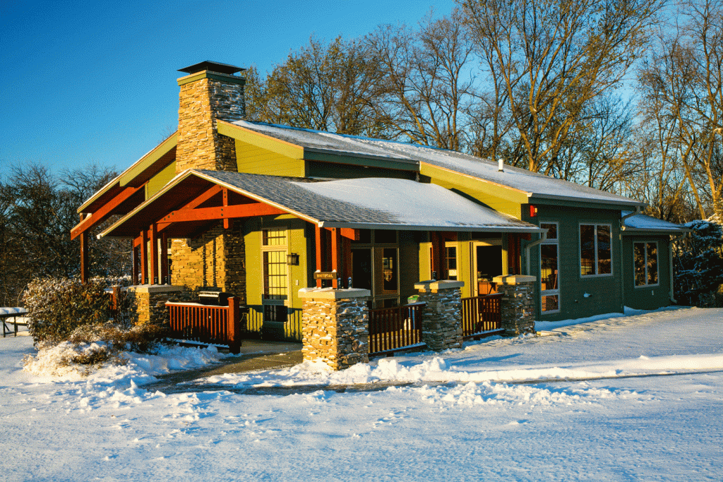 a green cabin with a stone fireplace pops against a blue sky in a white snow-covered landscape