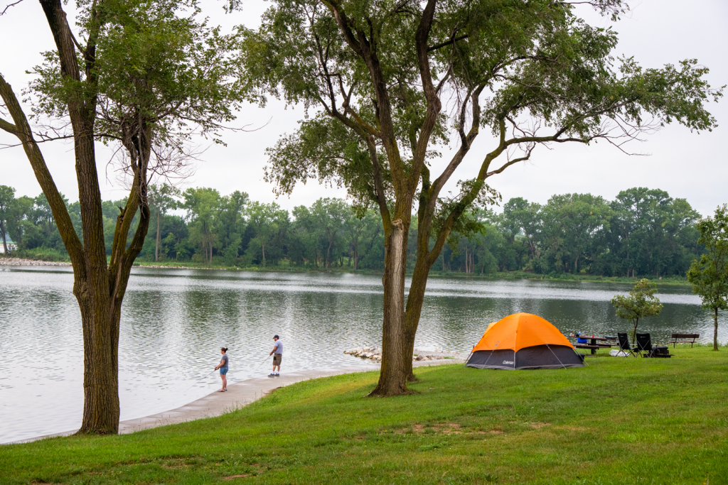 A couple fish from a new wall near their tent campsite at a lake during summer.