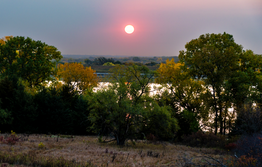 The sun rises over a tree-lined lake during fall.