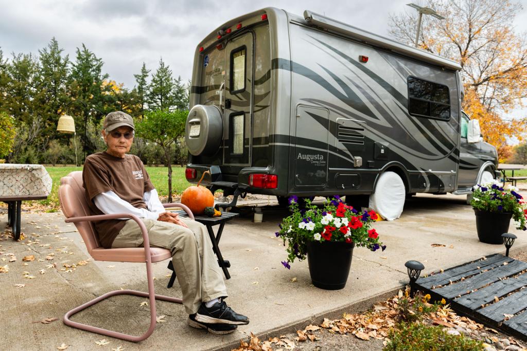 A campground host sits in a chair outside her camper at a park.