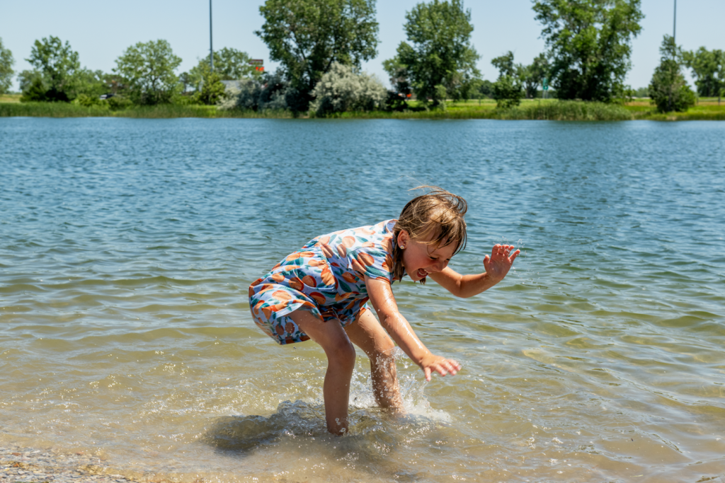 A little girl splashes playfully in the shallows of a small lake.