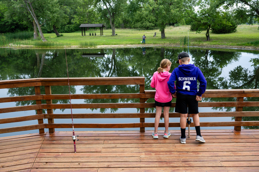 Two kids stand on a fishing pier and bait their fishing line during summer.